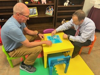 two men sitting at children's table  looking at AT for kids